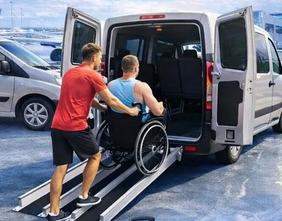 Chofer ayudando a un pasajero en silla de ruedas a subir a la van por la rampa