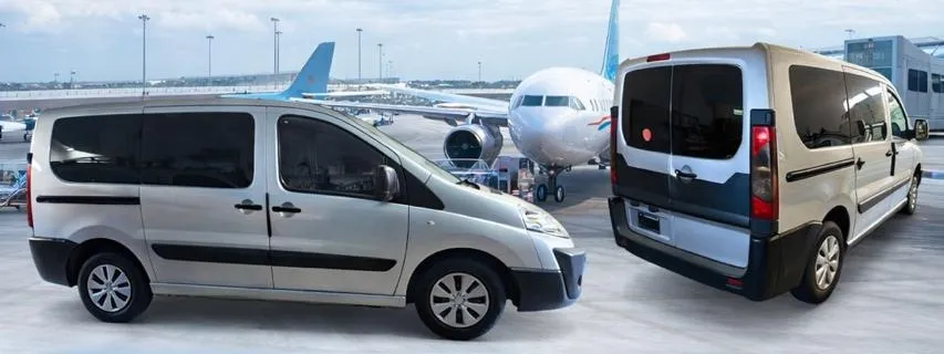 Van plateada de Traslados Aeropuerto frente a un avión en la pista